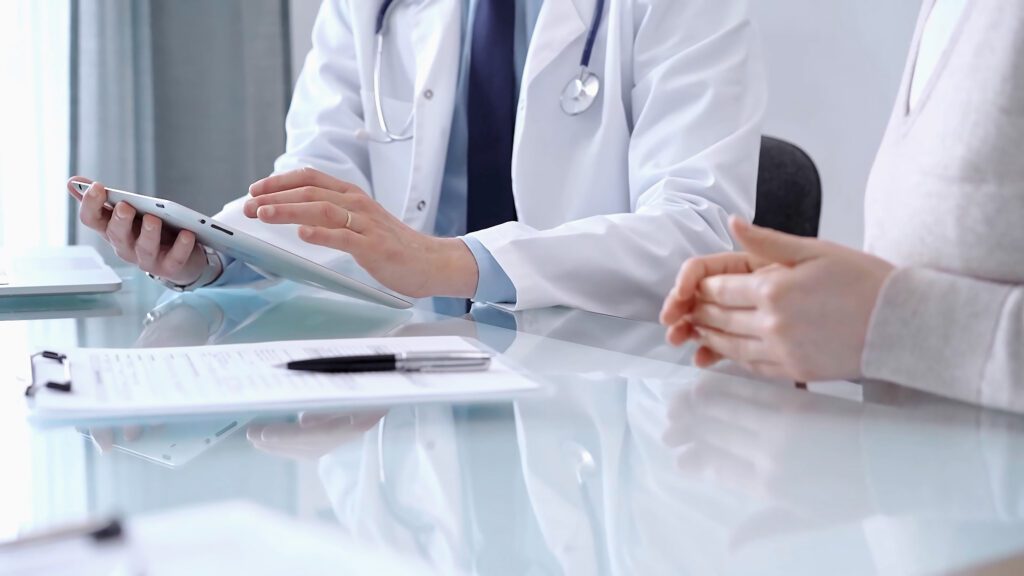 Doctor is consulting patient. Healthcare professional discusses medical information with a woman, using a tablet computer. Medicine