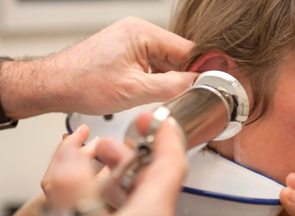 Doctor performing medical treatment, removing patient earwax wit