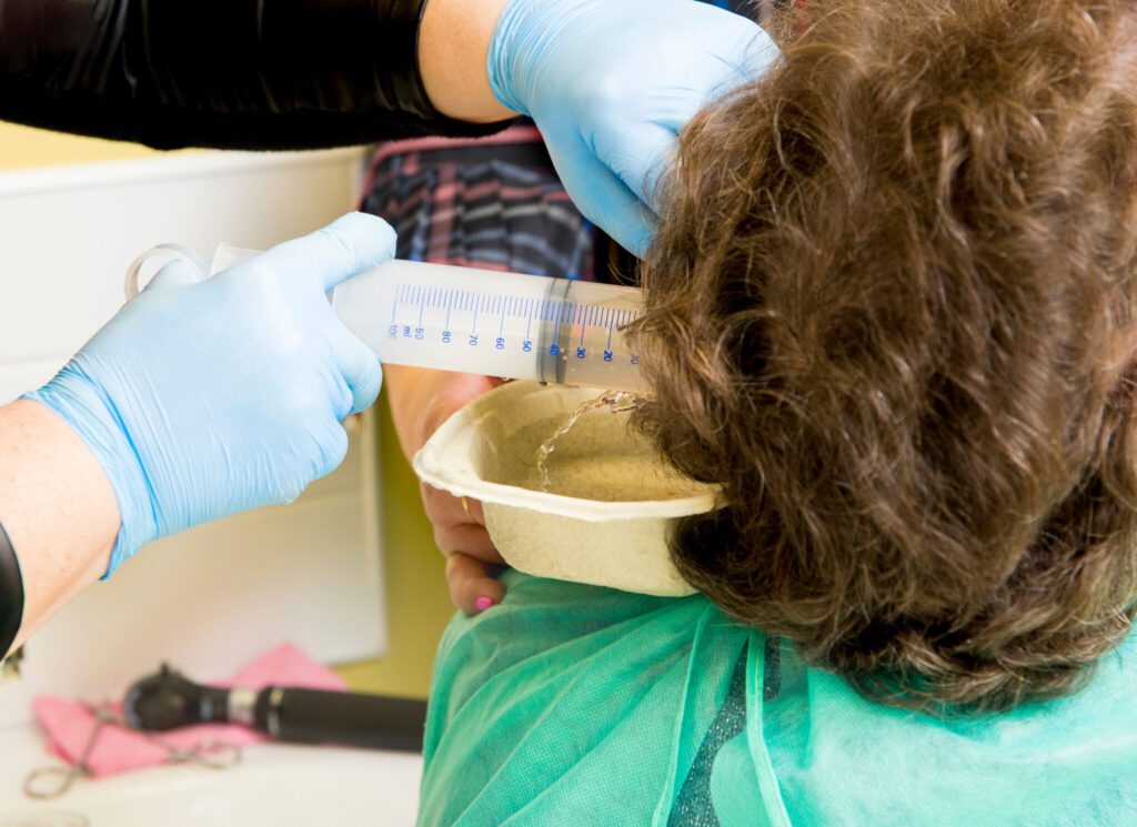 Doctor performing medical treatment, removing patient earwax wit