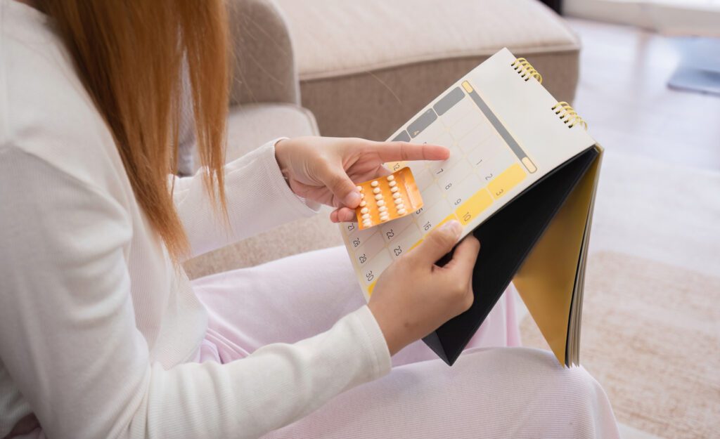 Young Woman Taking Birth Control Pills While Checking Calendar for Daily Dosage in a Modern Home Setting