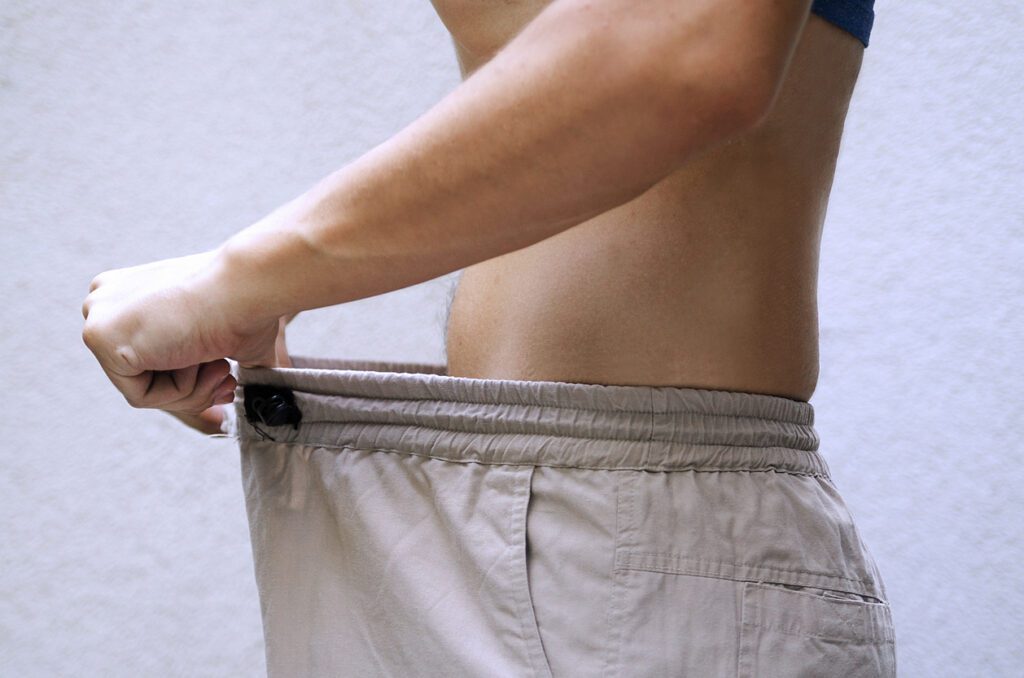 Young man showing how much he got his weight lost by pulling his pants.Guy checking size his genital