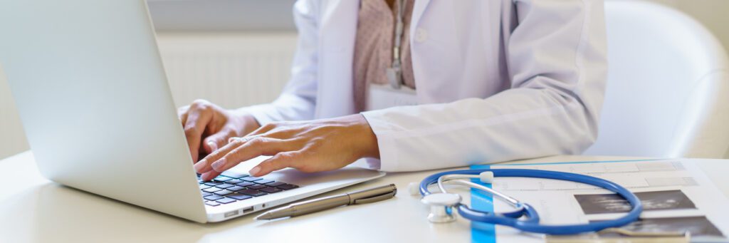 Panoramic banner with female doctor in white uniform working on laptop computer in hospital